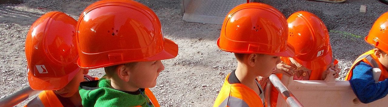 Vier Kinder mit Bauhelmen schauen einer Baustelle zu